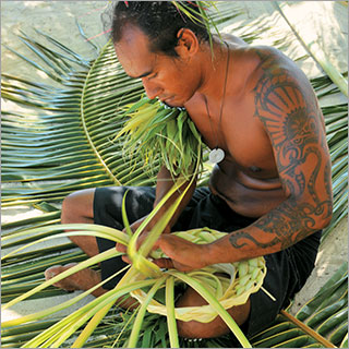 Native Polynesian male hand-weaving a palm leave basket.