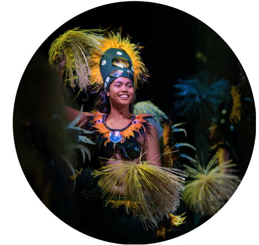 A Polynesian dancer performing in a traditional headdress and gown.