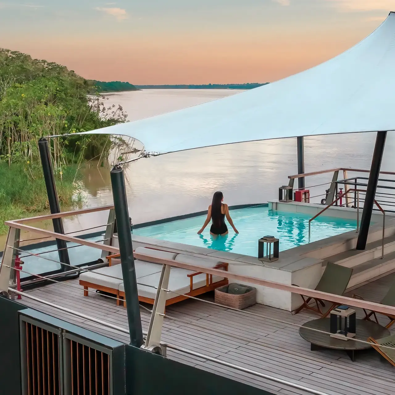 Aqua Expeditions | Woman in dipping pool overlooking white sand beach at sunset